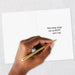 Hand holding a gold pen over a card with a motivational message on a light gray background