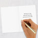Hand holding a gold pen over a white card with a message on a light gray background