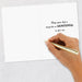 Hand holding a gold pen above a card with a motivational message on a light gray background