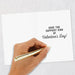 Hand holding a gold pen over a card with 'Have the Happiest Kind of Valentine's Day!' text on a light gray background