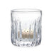 A clear glass candle holder containing two lit candles, casting a warm glow in a softly lit environment.