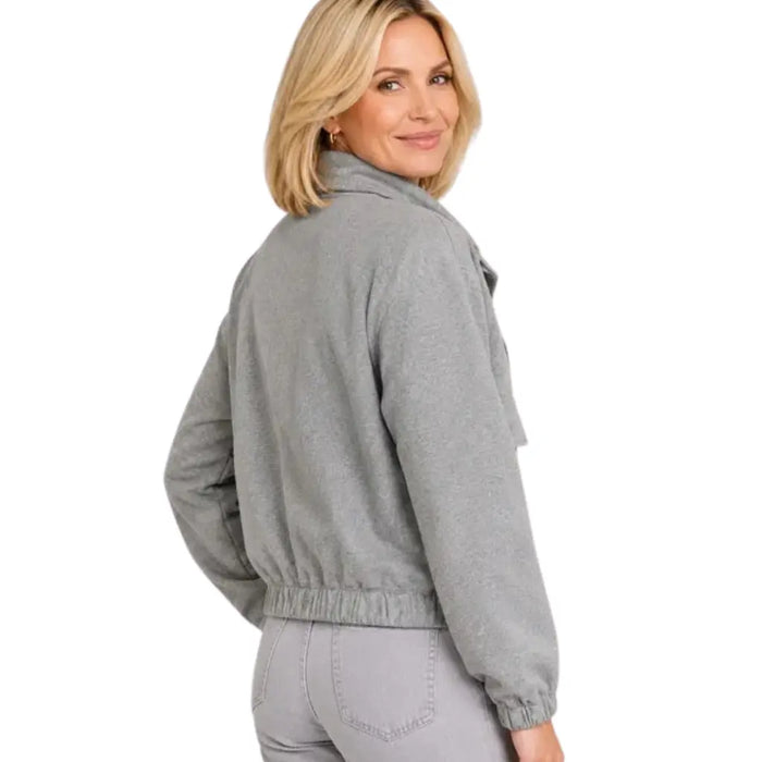 A woman wearing a light gray heathered fleece jacket with a high collar and elastic cuffs, shown from a three-quarters back view against a plain white background.