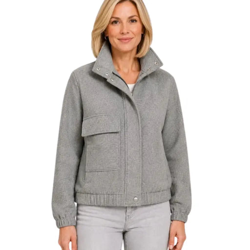 A woman wearing a light gray knit jacket with a high stand-up collar, snap-button front, and large front patch pockets, paired with light gray pants, against a plain white background.
