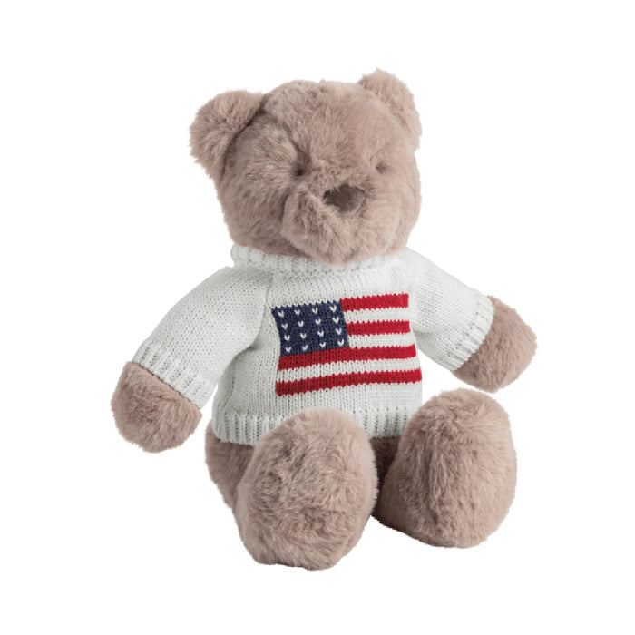 A teddy bear dressed in a sweater featuring the American flag, showcasing patriotic colors and design.