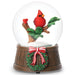 Snow globe with a red cardinal bird on a branch and a Christmas wreath on a wooden base.