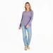 Woman wearing a purple long-sleeve shirt and light blue jeans on a white background