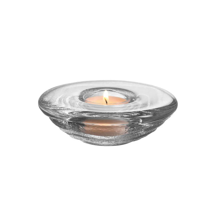 Clear glass  teas candle holder with a lit candle inside on a white background