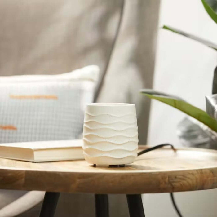White textured  sand stone candle warner on a wooden table with books and a plant in the background