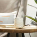 White textured  sand stone candle warner on a wooden table with books and a plant in the background