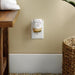 Decorative night light fragrance diffuser  on a wall next to a wooden table and woven basket with a plant.
