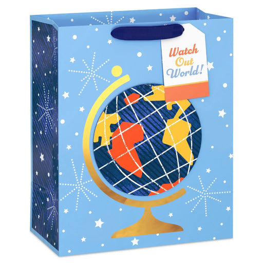 gift bag on a white background featuring a blue star-and-fireworks design with a colorful globe attachment on a gold stand and a “Watch Out World!” gift tag