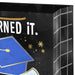 Close‑up of black graduation gift bag with blue cap and gold accents