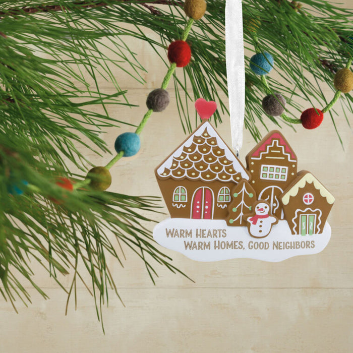 Decorative Christmas ornament with gingerbread houses and a snowman on a branch.