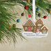 Decorative Christmas ornament with gingerbread houses and a snowman on a branch.