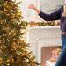 Person decorating a Christmas tree with lights and ornaments in a festive living room.