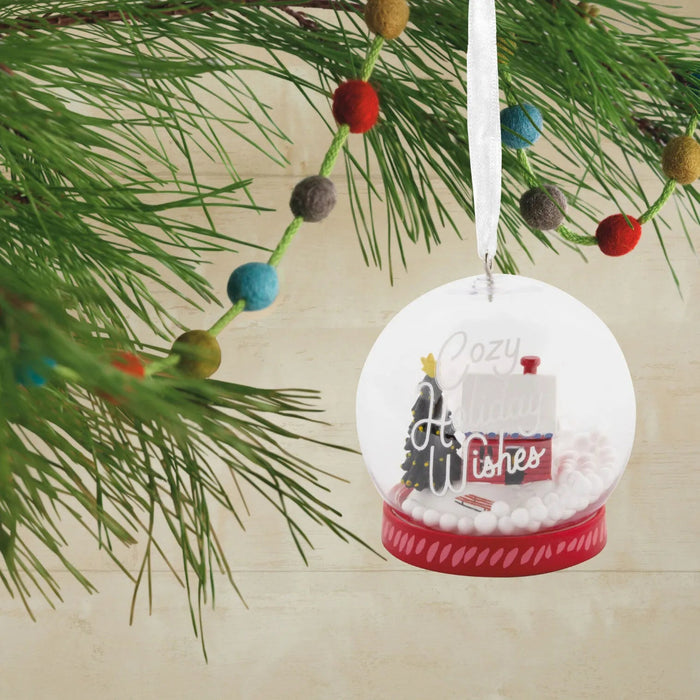 Hallmark Cozy Holiday Wishes Snow Globe Christmas ornament featuring a red log cabin, snowy roof, decorated evergreen tree, and swirling white snowballs.
