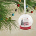 Hallmark Cozy Holiday Wishes Snow Globe Christmas ornament featuring a red log cabin, snowy roof, decorated evergreen tree, and swirling white snowballs.