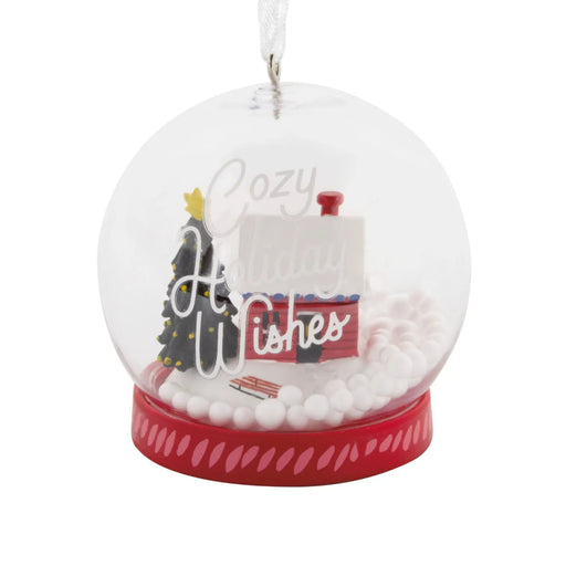 Hallmark Cozy Holiday Wishes Snow Globe Christmas ornament featuring a red log cabin, snowy roof, decorated evergreen tree, and swirling white snowballs.