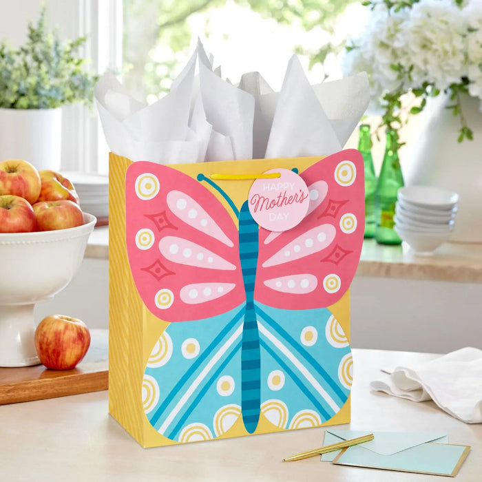 Large yellow Mother’s Day gift bag with pink and blue butterfly design displayed on a table beside a greeting card