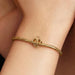 Gold bracelet with a heart charm on a wrist against a neutral background