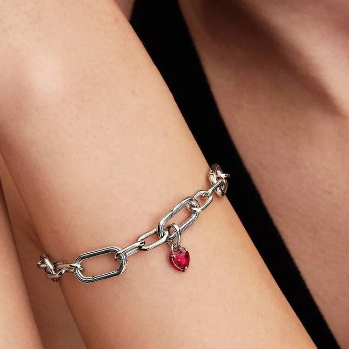 Silver chain bracelet with a red heart charm on a wrist against a neutral background