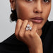 Close-up of a woman's hand wearing a floral ring and a earring with a neutral background