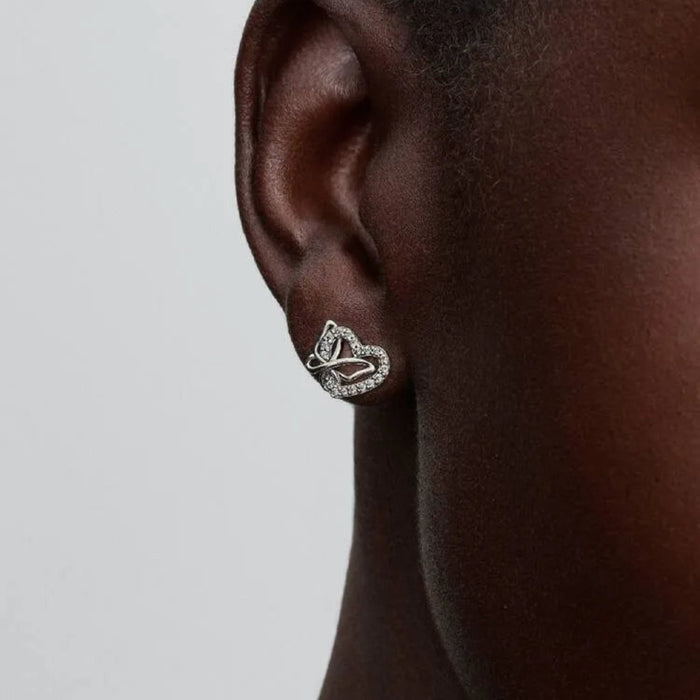 Close-up of a woman wearing a heart and butterfly shaped earring with a neutral background