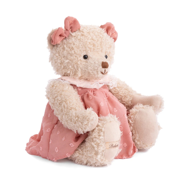  A teddy bear wearing a pink dress is positioned on a white background.