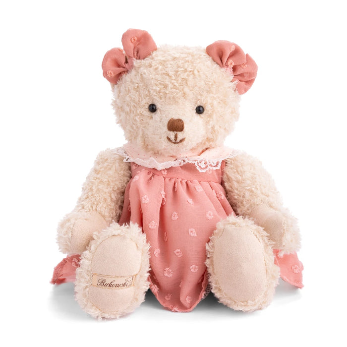 A teddy bear dressed in a pink dress sits against a plain white background.