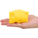 Yellow cheese-shaped block held in a hand against a white background