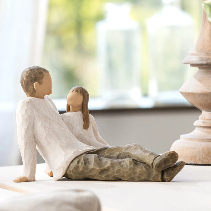 Decorative sculpture of a father and daughtersitting together on a surface with a blurred background