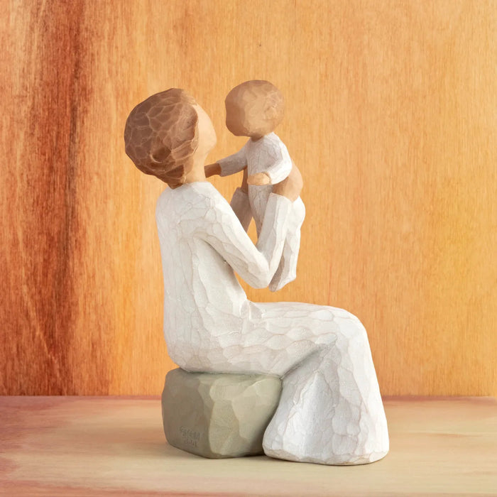 Willow Tree Grandmother figurine holding a baby side view with a amber background. 