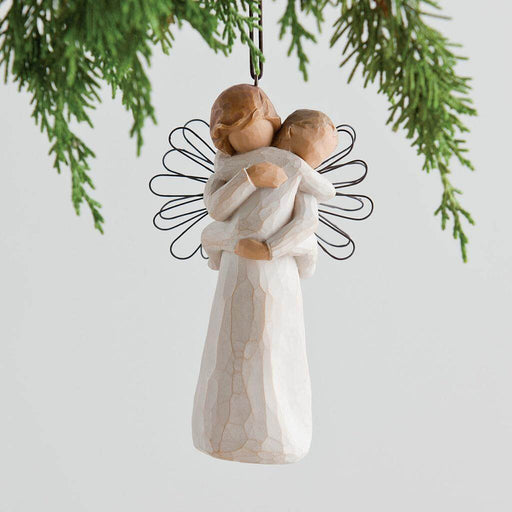 Decorative angel ornament holding a child, hanging from a branch on a light background