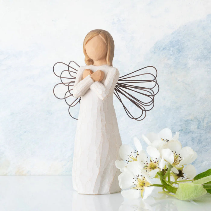 Angel figurine with open wings holding her heart, surrounded by white flowers on a light background