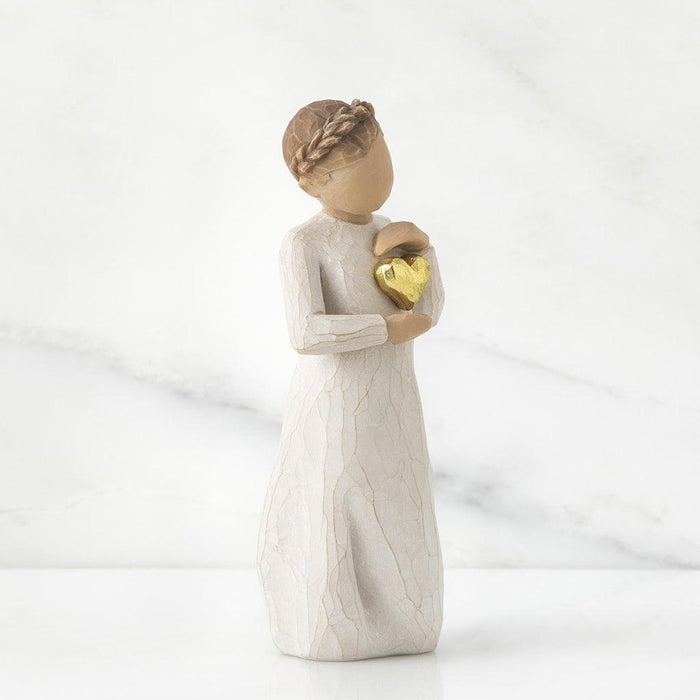 Figurine of a woman holding a gold heart against a white background
