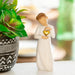 Angel figurine holding a gold heart next to a potted plant on a blurred background