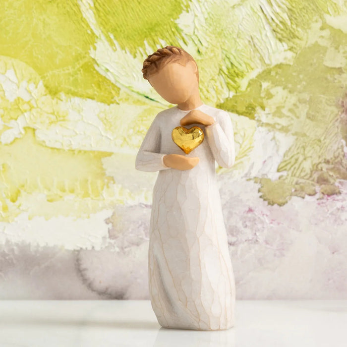 Angel figurine holding a gold heart against a colorful abstract background
