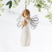 Angel figurine with wire wings hanging against a light background with greenery