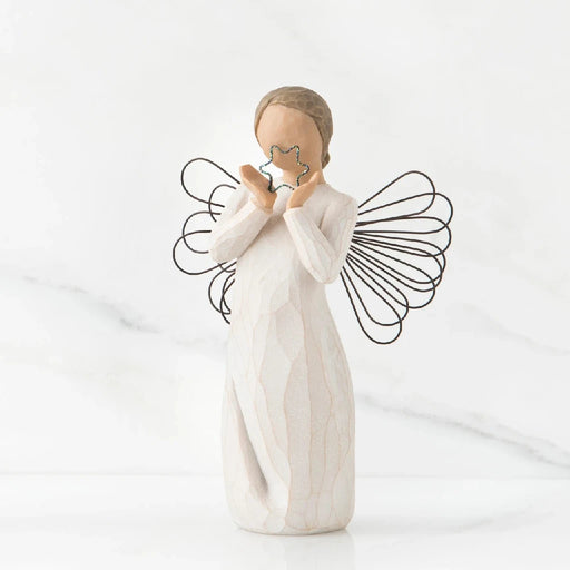 A willow tree angel holding a heart, symbolizing love and serenity in a peaceful outdoor setting.