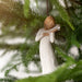 A willow tree angel holding a small bird, surrounded by soft greenery and a serene atmosphere.