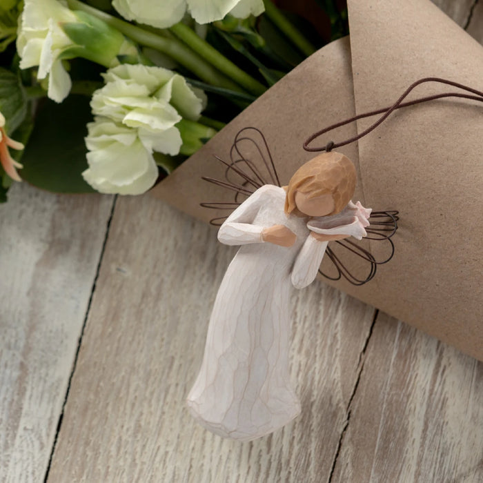 A delicate angel made of willow branches cradles a bird, set against a tranquil natural backdrop.