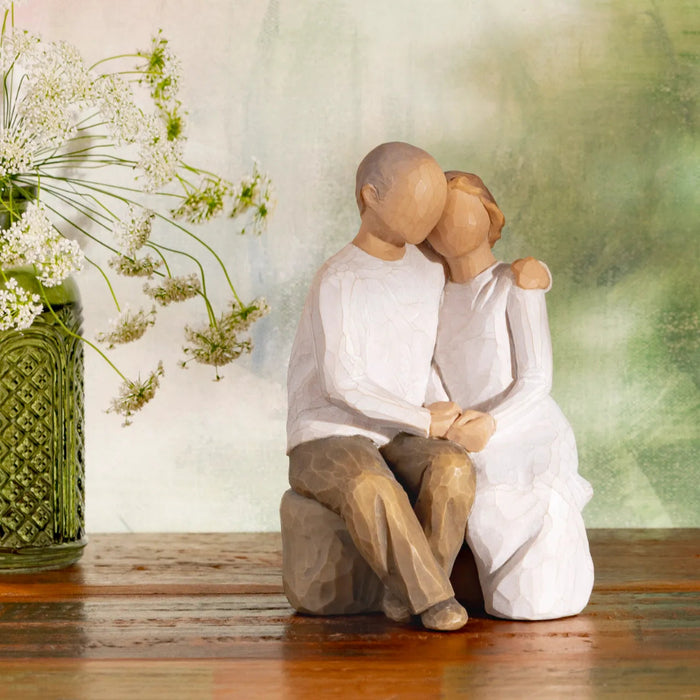 Statue of a couple embracing with a vase of flowers on a wooden surface