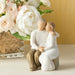 Decorative figurine of a couple embracing with a vase of flowers in the background.