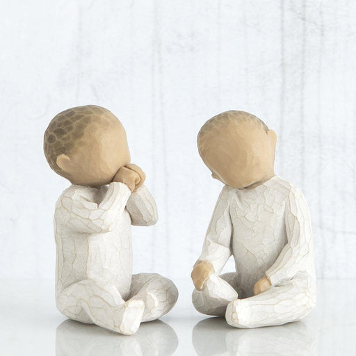 Two ceramic figures of children sitting and facing each other on a white background
