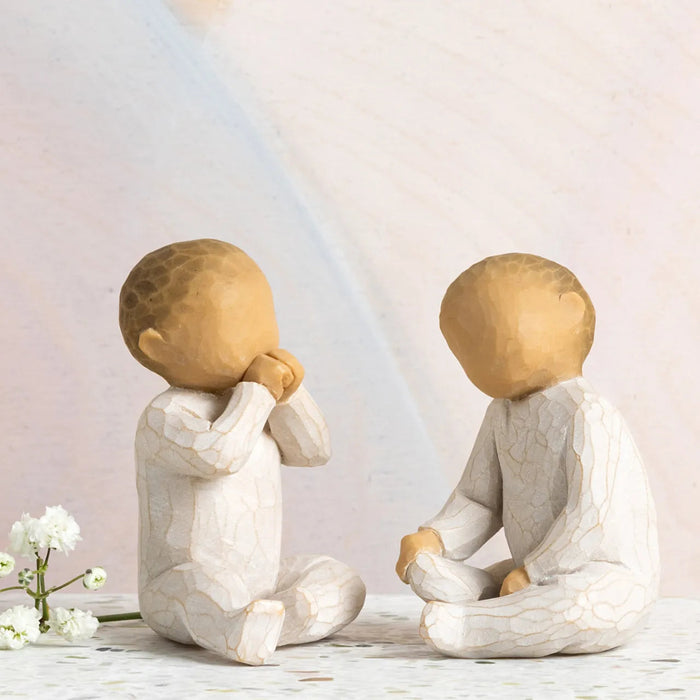 Two stone sculptures of children sitting on a surface with a light background