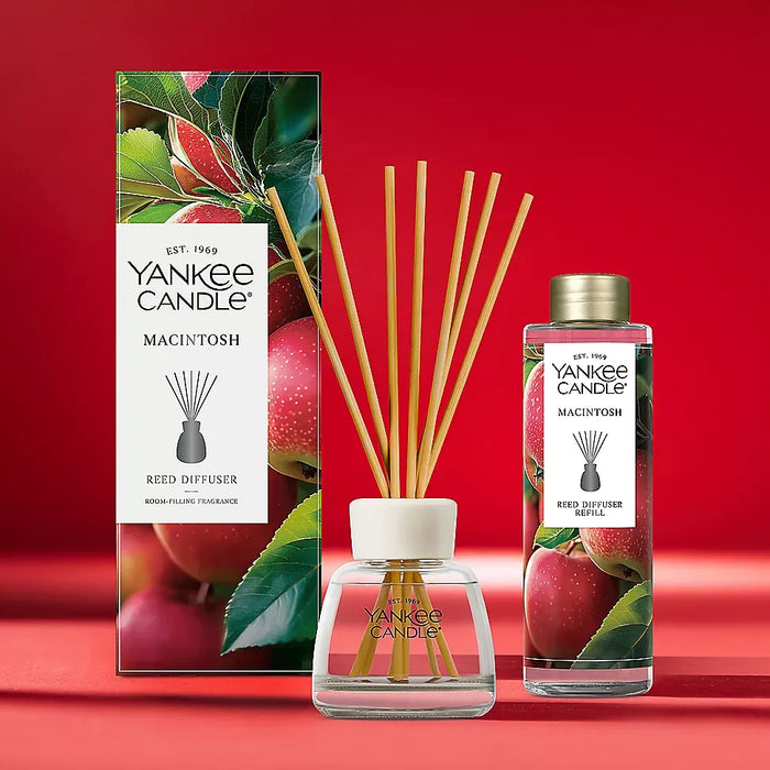 Yankee Candle Macintosh reed diffuser set with a glass reed diffuser bottle, wooden reeds, a matching branded bottle, and the printed product box on a red studio background.