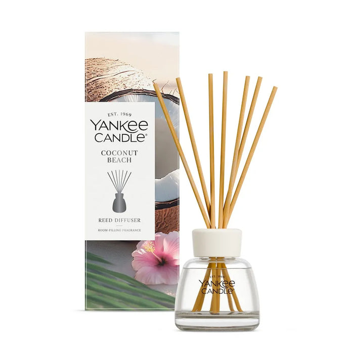 Yankee Candle Coconut Beach reed diffuser with a glass bottle, white cap, and natural wood reeds, shown in front of its printed packaging box on a white background.