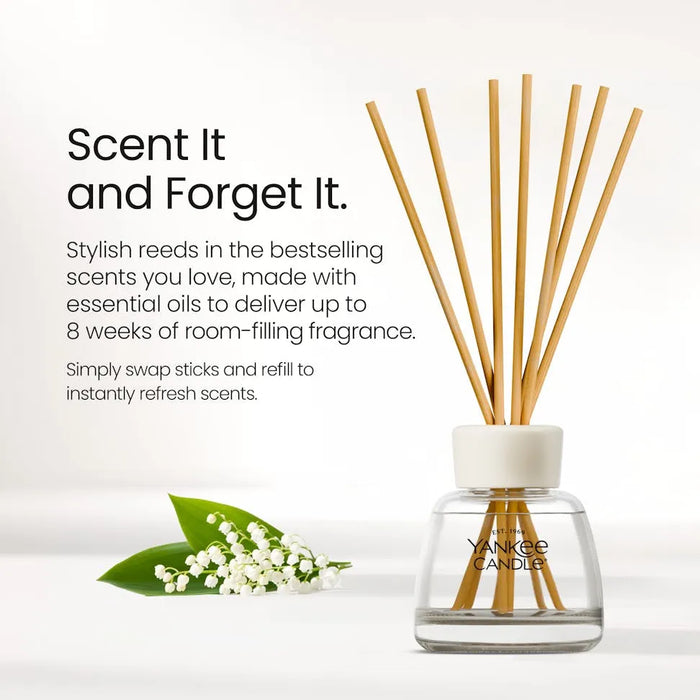 Yankee Candle reed diffuser bottle with wooden reeds, shown on a clean white background with promotional text and a small lily of the valley sprig.