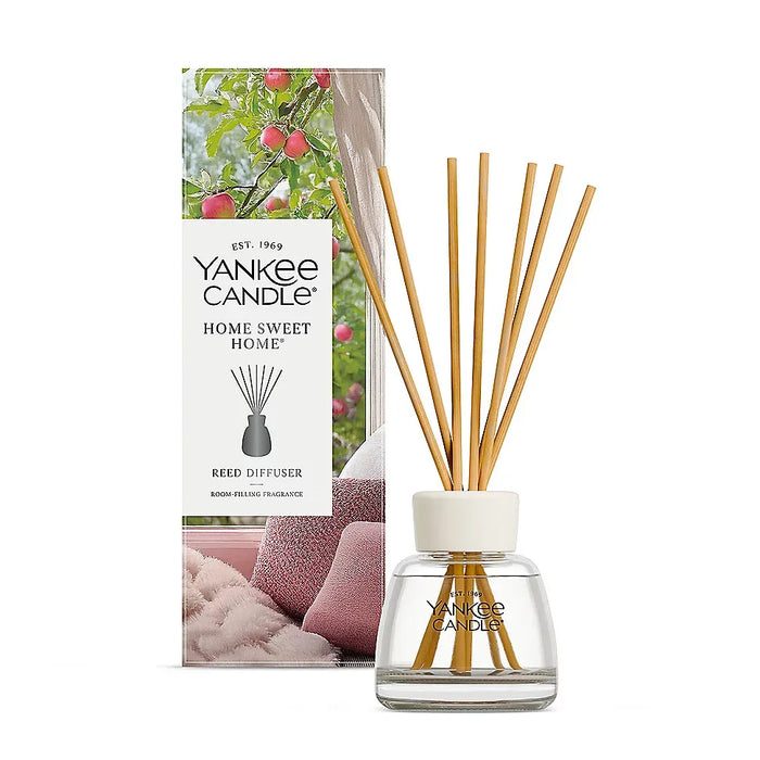 Yankee Candle Home Sweet Home reed diffuser with natural wood reeds in a clear glass bottle, shown in front of its illustrated packaging box on a white background.