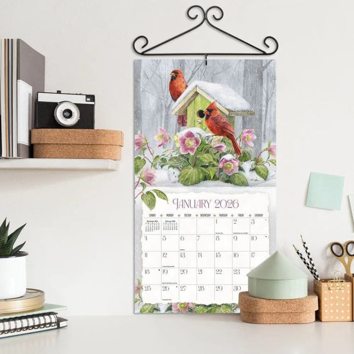 Calendar with a winter scene featuring cardinals and flowers, displayed on a shelf.
